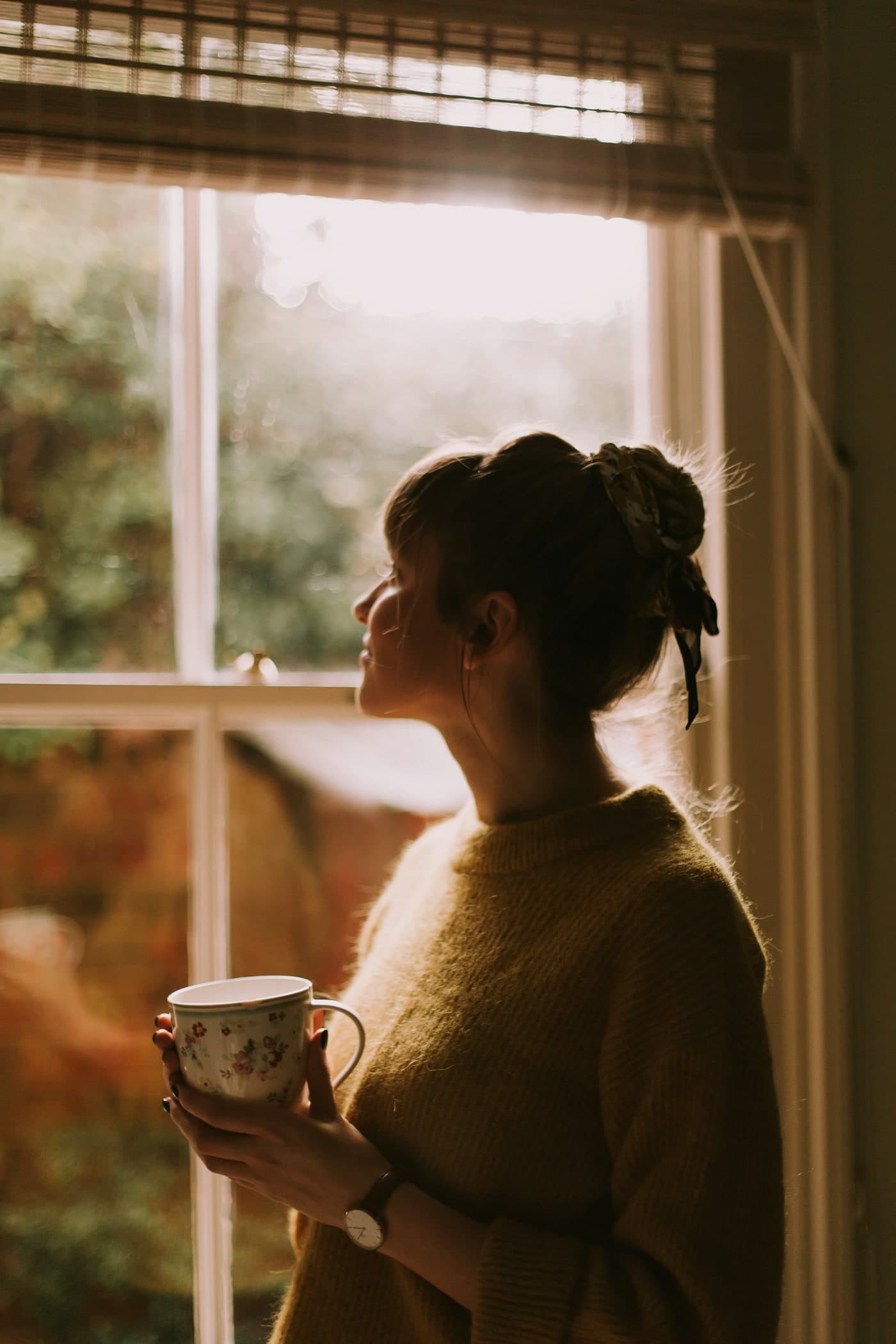 Woman by a window holding a mug, soft morning light