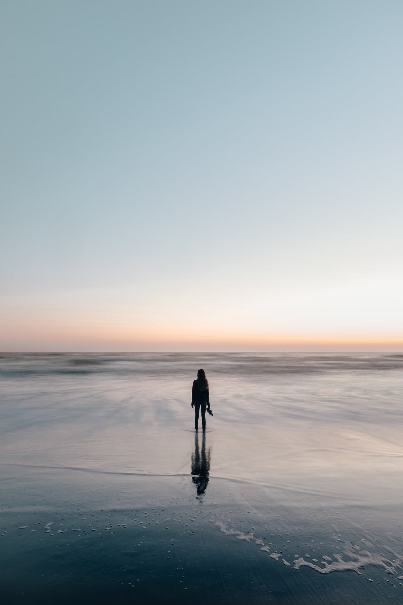 Woman standing alone at the shoreline at dusk